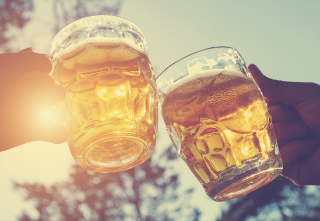 People holding glass mugs of beer, toasting, with sunlight shining through