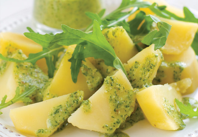 Potato wedges on a white plate with green vinaigrette, garnished with arugula