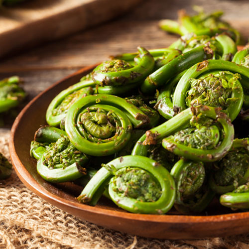 A mountain of fiddleheads served on a wooden plate