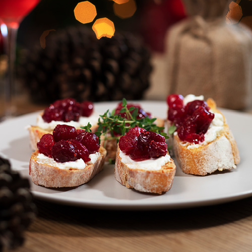 A white plate with 6 pieces of bread, topped with ricotta and cranberry mixture.